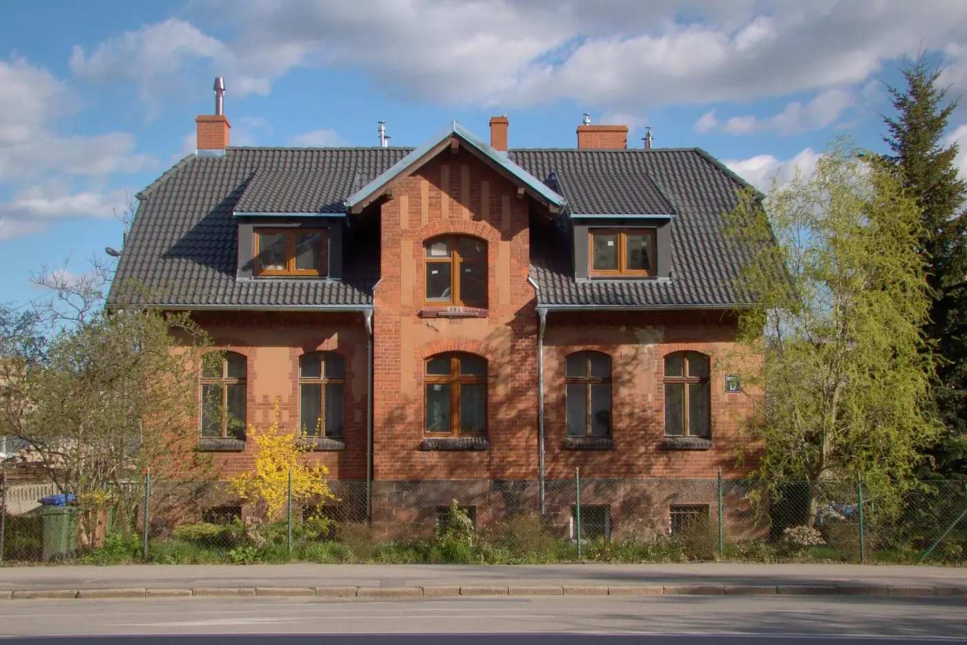 Zweigeschossiges Backsteinhaus mit dunklem Dach, Gauben und Vorgarten an einer Straße (Neuenkirchen, Landkreis Osterholz)
