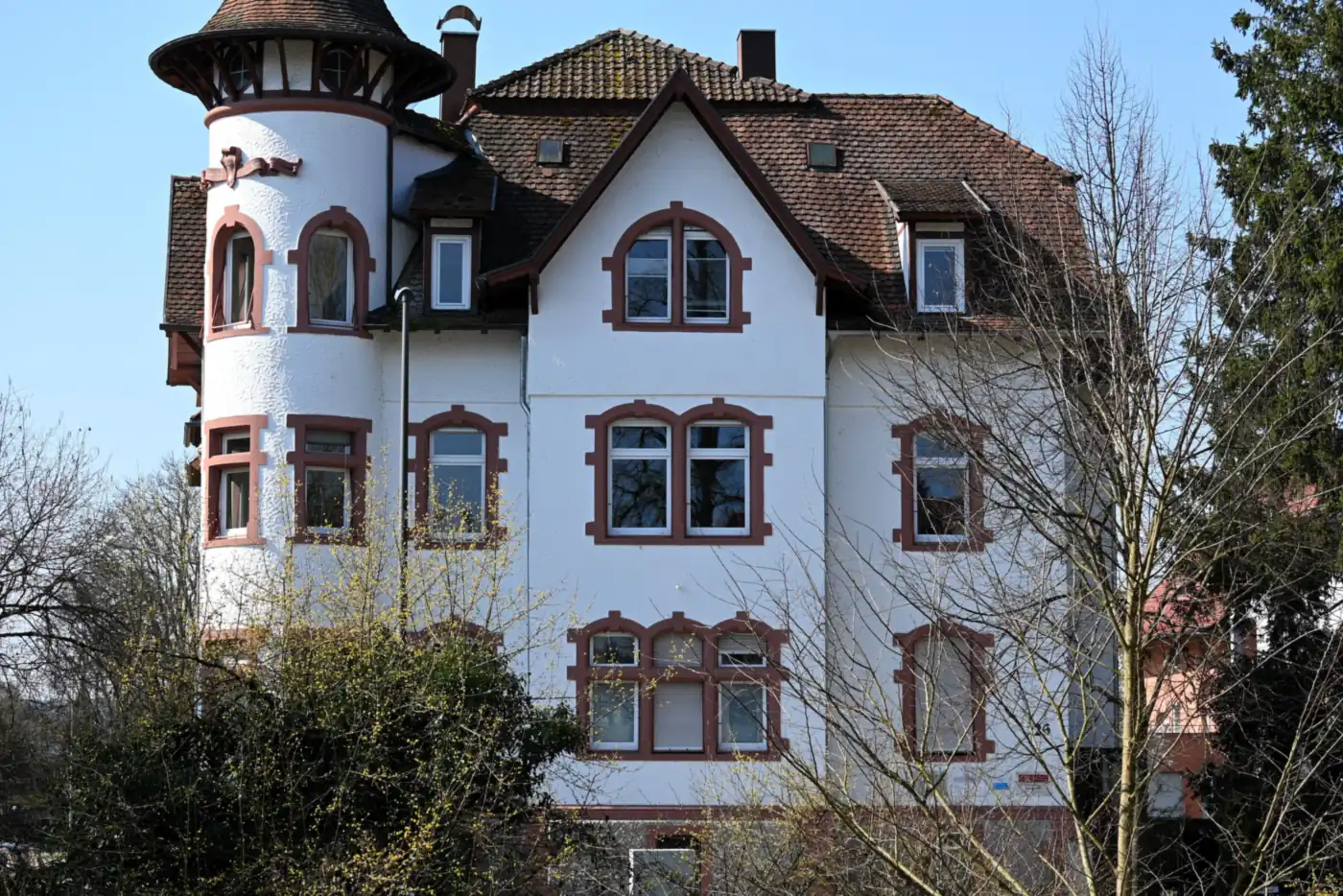 Weiße Jugendstilvilla mit Rundturm und rotbraun gefassten Fenstern hinter kahlen Bäumen (Westerhorn, Kreis Pinneberg)