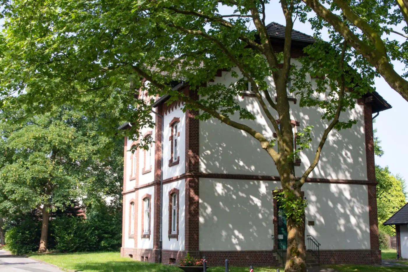 Weiß verputztes Haus mit Backsteingliederung im Schatten eines großen Laubbaums (Schwabach)