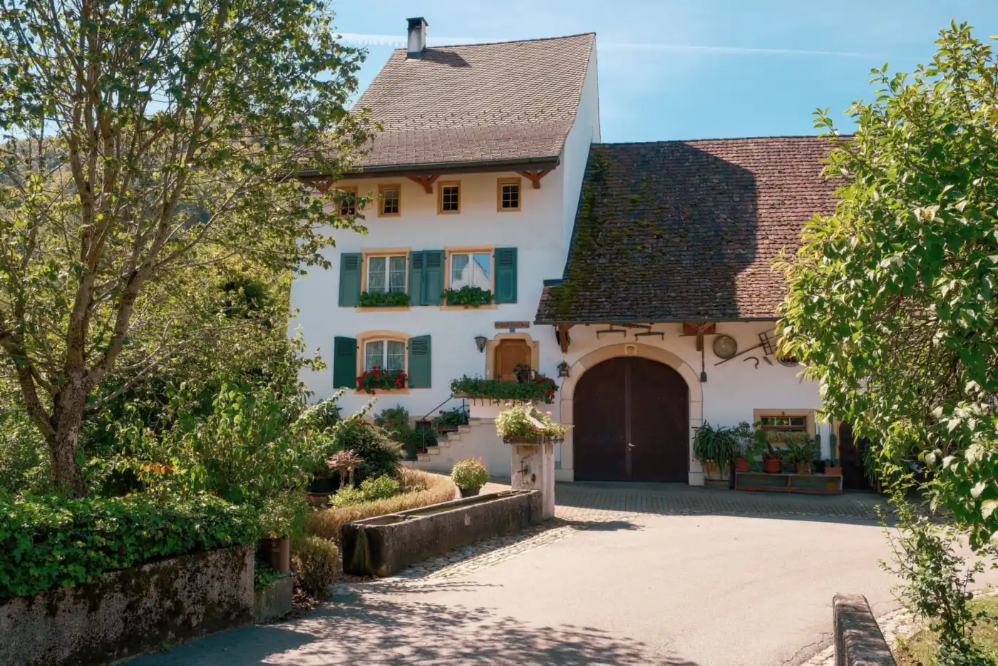 Weiß verputztes Bauernhaus mit grünen Fensterläden, Blumenkästen und rundbogigem Scheunentor (Born, Vorpommern-Rügen)