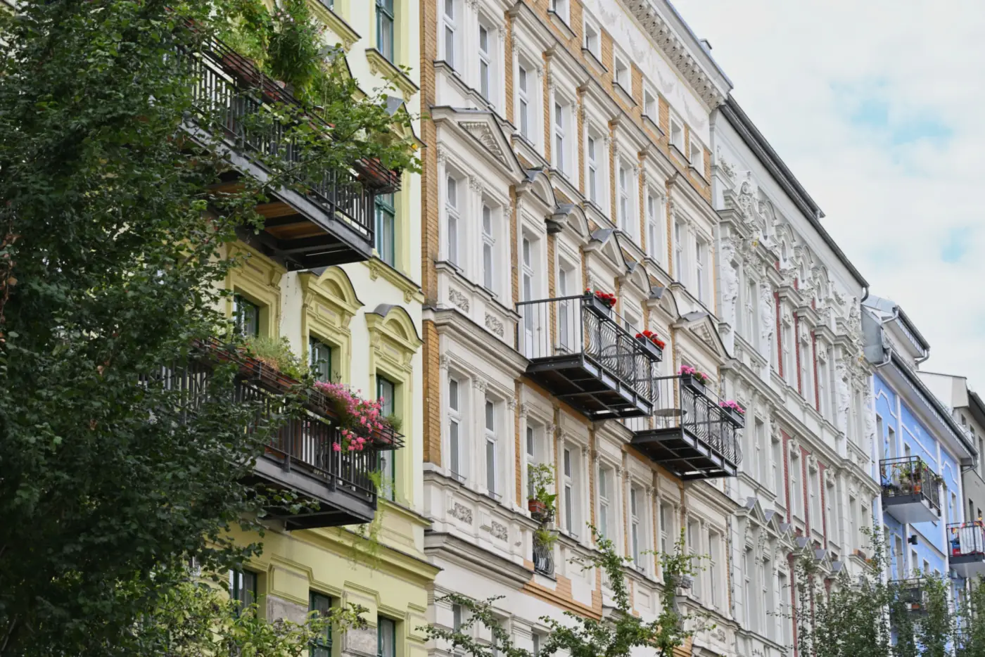 Gründerzeithäuser mit hellen Stuckfassaden und bepflanzten Balkonen an einer Stadtstraße