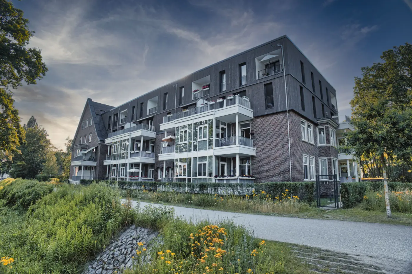 Modernes Mehrfamilienhaus aus dunklem Klinker mit hellen Balkonen an einem Fußweg