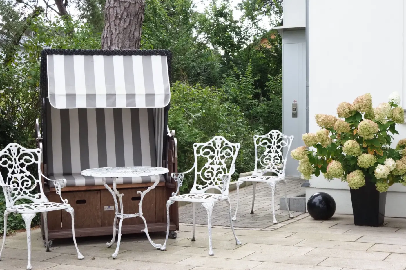 Terrasse mit gestreiftem Strandkorb, weißen Gartenstühlen und blühenden Hortensien (Efringen-Kirchen, Landkreis Lörrach)