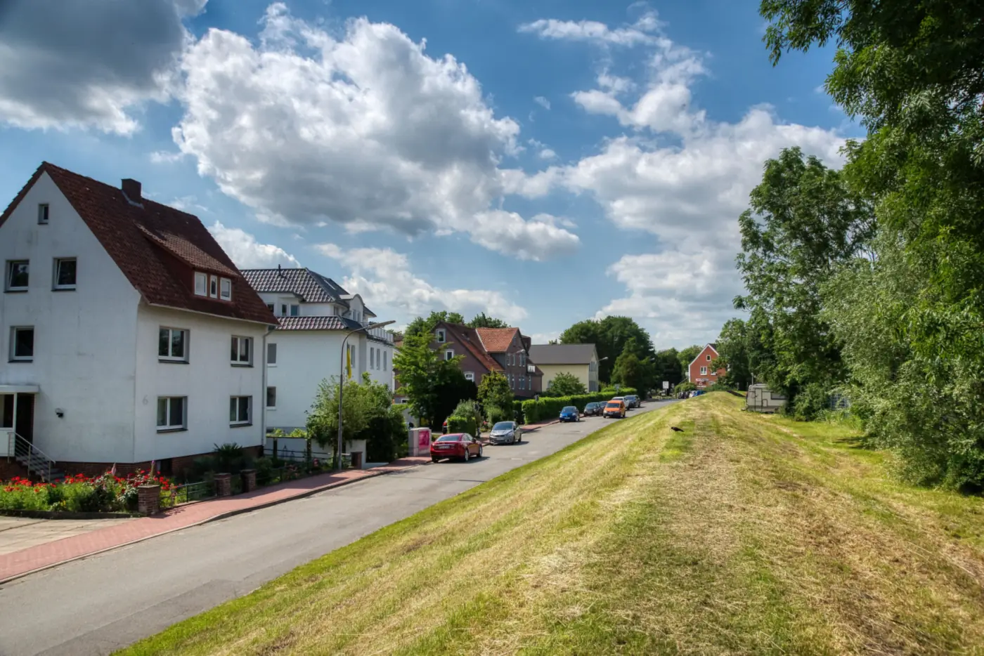 Wohnstraße mit weiß verputzten Häusern, parkenden Autos und gemähter Grasböschung (Herborn, Lahn-Dill-Kreis)