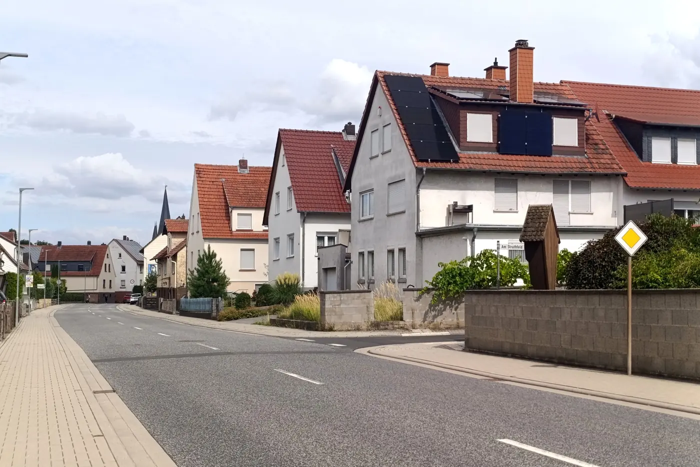 Ortsstraße mit hellen Einfamilienhäusern, roten Ziegeldächern und Solarmodulen (Hohenfelde, Kreis Steinburg)