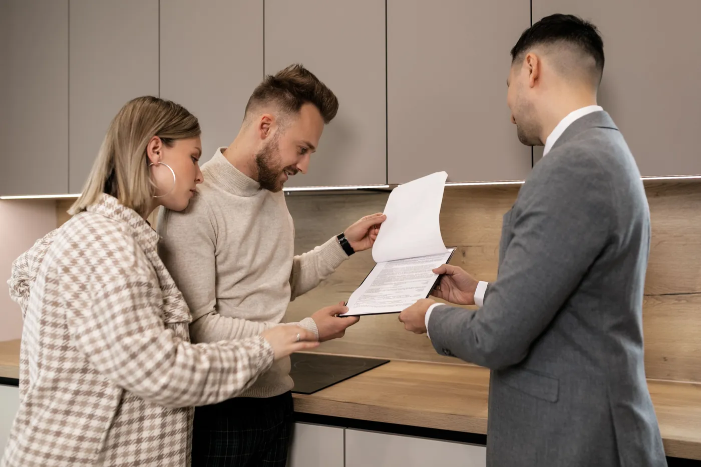 Makler zeigt einem Paar in der Küche ein mehrseitiges Dokument (Lustadt, Landkreis Germersheim)