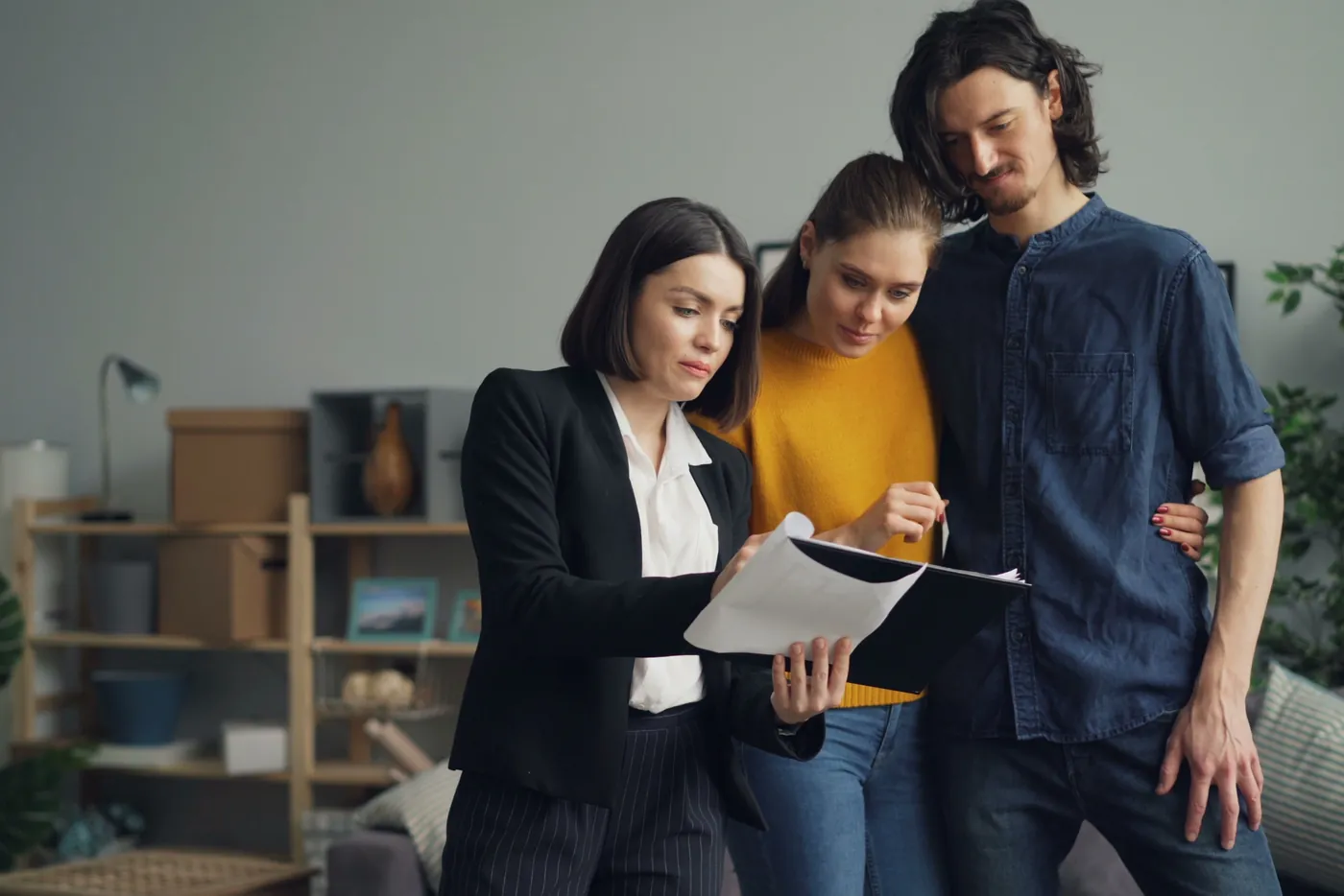 Maklerin geht mit einem Paar im Wohnzimmer eine Mappe mit Unterlagen durch (Osterwieck, Landkreis Harz)