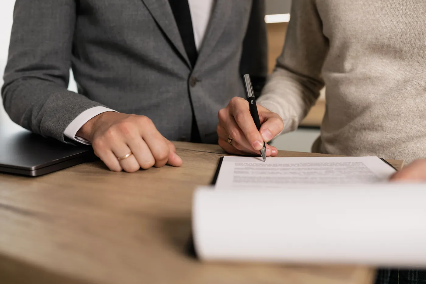 Kunde unterschreibt am Holztisch ein Dokument, daneben der Berater im grauen Sakko (Winnweiler, Donnersbergkreis)